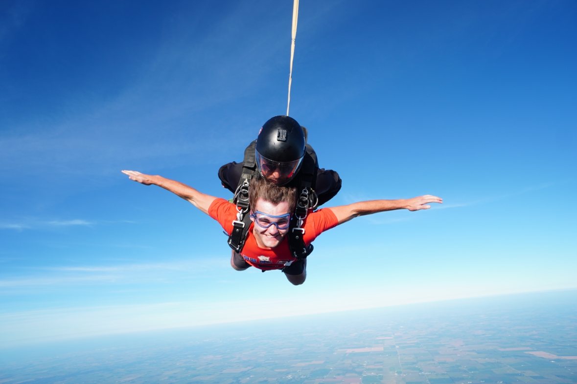 Michael Greenlee in free fall during a tandem skydive, arms spread, high above farmland