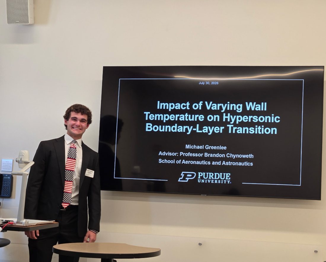 Michael Greenlee standing next to a screen showing his presentation title, Impact of Varying Wall Temperature on Hypersonic Boundary-Layer Transition